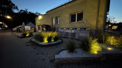 Seitliche Außenansicht des Vorderhauses mit beleuchteten Pflanzbeeten und Vorplatz